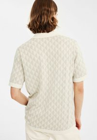 Korte mouw shirt in lichtbeige met een gestructureerd ruitpatroon en contrasterende kraag. Heeft een ontspannen pasvorm en zachte stof.