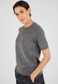 Maglione grigio a maniche corte in maglia con dettagli a coste sui lati e orlo. Tessuto morbido, scollo rotondo e vestibilità comoda. Abbinato a pantaloni scuri.