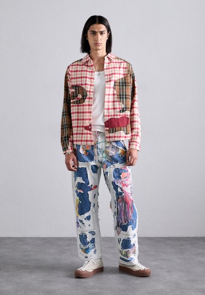 Men's plaid shirt in red and beige with contrasting patches; paired with distressed denim jeans featuring colorful patterns and a relaxed fit.