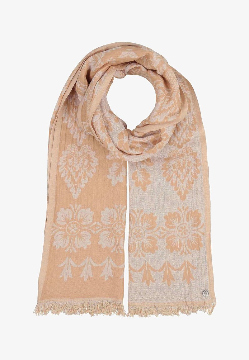 Écharpe beige clair avec des motifs floraux et feuillus complexes, bords à franges et petite étiquette métallique circulaire dans un coin.