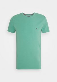 Vihreä puuvillasta valmistettu lyhythihainen t-paita, jossa on pyöreä kaula-aukko. Paidassa on pieni logo vasemmassa rinnassa ja erottuva raidallinen yksityiskohta kaula-aukossa.