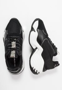 Black and silver athletic sneakers with mesh and textile upper, thick white rubber sole, and branded accents on the tongue and side.