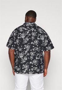 Kortärmad skjorta i svart tyg med ett vitt blommönster. Lösen passform med klassisk krage och rak nederkant.