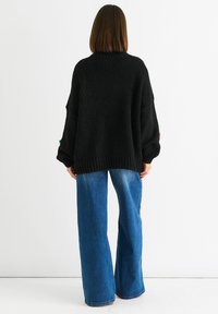 Czarny, oversize sweter z dzianiny o fakturowanym wykończeniu i opadającymi ramionami, zestawiony z szerokimi niebieskimi dżinsami.