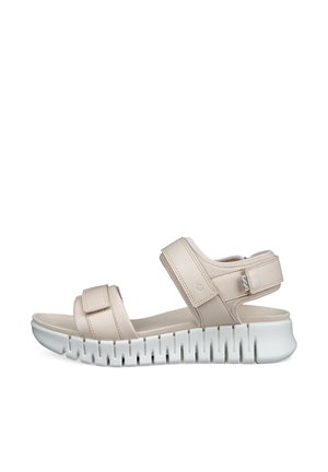 Sandale beige à bout ouvert avec deux brides réglables et une semelle épaisse blanche rainurée pour plus de confort et d'adhérence.