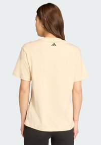 Beige színű, rövid ujjú póló, pamutból készült, kerek nyakkal és egy apró fekete Adidas logóval a váll közelében. Sima tapintású.