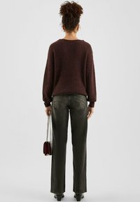 Bordowy sweter o fakturze, szerokie rękawy, w połączeniu z wysokim stanem ciemnoszarych dżinsów i małą bordową torebką, stojący na neutralnym tle.