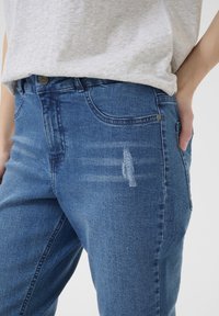 Blå denimjeans med slim fit, med blekta partier och en lätt slitage detalj. Klassisk femficksdesign med knappstängning framtill.