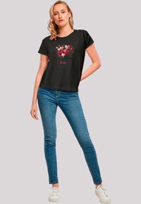 Black t-shirt featuring a colorful heart graphic and text "Be Mine". Paired with light blue skinny jeans and white sneakers.