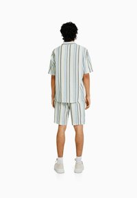 Camiseta de manga corta a rayas y pantalones cortos a juego en azul claro, blanco y negro. La tela parece tener textura; conjunto diseñado para uso informal.