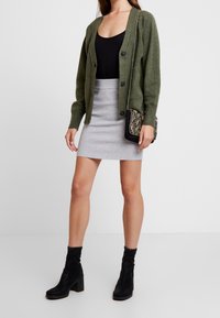 Olivgrön stickad kofta med knappar, matchad med en ljusgrå kroppsnäv kjol. Svarta ankelstövlar och en mönstrad kuvertväska med axelrem.