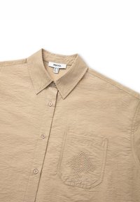 Beige collared shirt featuring a textured fabric, front buttons, and a pocket with a distinctive perforated pattern.