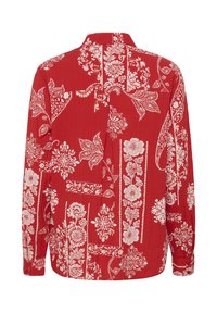 Pikkade varrukatega punane särk valgete lille- ja paisleimustritega, millel on krae ja nööbitavad mansetid, kujutatud tagantpoolt.