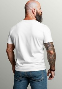 White short-sleeve t-shirt with a round neckline, worn with blue denim jeans. Notable tattoos visible on the right arm.