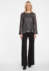 Zwarte top met lange mouwen, voorzien van een gestructureerd patroon en glanzende accenten. Gecombineerd met zwarte, wijde broek met subtiele versieringen.