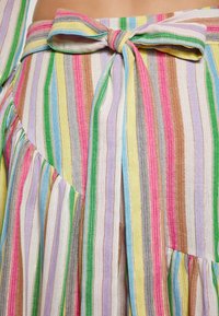 Tessuto a righe multicolori con tonalità di rosa, giallo, verde e blu. Presenta un fiocco in vita e dettagli plissettati.