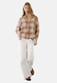 Kariertes Hemd in Beige- und Rosttönen, kombiniert mit lockeren weißen Hosen. Das Hemd hat eine lockere Passform und lange Ärmel.