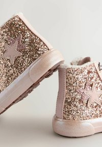Baskets montantes roses pailletées avec accents en étoile ; des sequins recouvrent le dessus, avec une semelle en caoutchouc texturée et une doublure en polaire à la cheville.