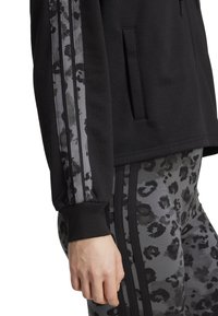 Felpa nera con strisce laterali a stampa leopardata grigia. Tessuto morbido, vestibilità comoda, con tasca frontale e polsini a coste. Abbinata a leggings coordinati.