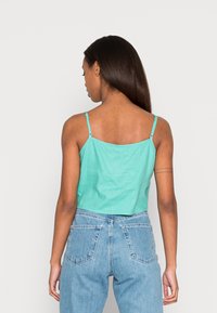 Top cropped turquesa com alças finas e ajustáveis. Apresenta uma textura suave e um design simples e clássico. Usado com jeans de cintura alta.