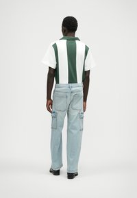 Zöld és fehér csíkos, rövid ujjú póló, világoskék cargo farmernadrággal párosítva, amely oldalzsebekkel és laza szabással rendelkezik.