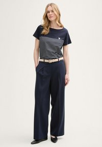 Camiseta de rayas marinas con mangas cortas, combinada con pantalones anchos navy y un cinturón beige. Zapatos negros completan el conjunto.