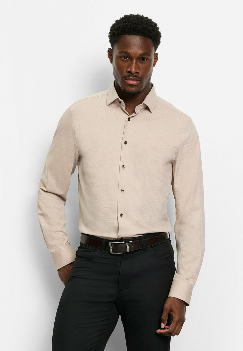 Beige Langarmhemd mit strukturiertem Muster, Button-Down-Kragen und dunklen Knöpfen, getragen mit schwarzen Hosen und einem braunen Gürtel.