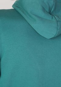 Teal hoodie med en mjuk, slät textur, med en avslappnad passform och en dragsnodd vid huvudet. Tyget verkar lätt och bekvämt.