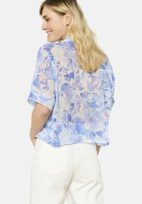Trumpas rankovėmis, lengvas bliusonas iš permatomos medžiagos, su mėlyna gėlių raštu lengvame fone, susukti rankogaliai ir šiek tiek trumpintas apatinis kraštas.