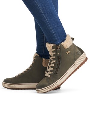 Baskets montantes vert olive avec doublure en fourrure beige, fermeture éclair sur le côté et semelle en caoutchouc texturé. Comprend des lacets et des détails de coutures contrastées.