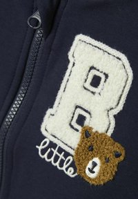 Námornícka zipová mikina s plyšovým bielym nášivkom "B" a aplikovanou tvárou hnedého medveďa. Mäkká tkanina s detailným vyšívaním.