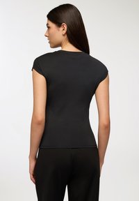 Czarna dopasowana koszulka z krótkimi rękawami, gładka w dotyku, z okrągłym dekoltem, w połączeniu z czarnymi spodniami, widok z tyłu.