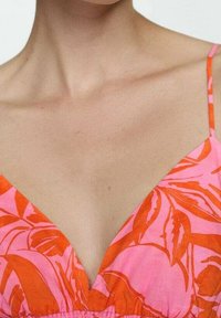 Robe rose et orange avec un décolleté plongeant en V, ornée de motifs de feuilles. Fines bretelles et tissu léger créent un style décontracté.