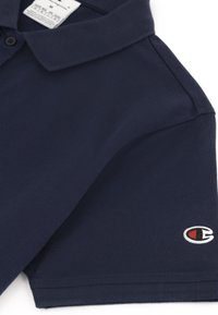 Polo bleu marine en coton texturé avec une patte de boutonnage à trois boutons, des manches courtes et un petit logo brodé sur la poitrine.
