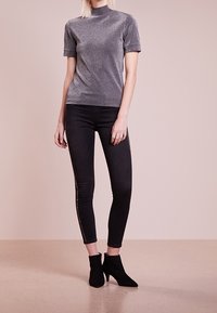 Top gris de manga corta y cuello alto en una tela texturizada, combinado con jeans skinny negros con detalles laterales y botas negras hasta el tobillo.