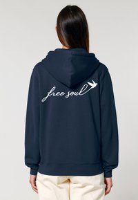 Felpa navy con tasca a kangaroo, cappuccio regolabile con cordino e testo "free soul" con un grafico di uccello sul retro. Tessuto morbido e testurizzato.