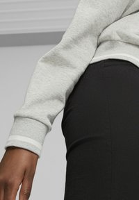 Felpa grigia con polsini a coste e strisce bianche, abbinata a pantaloni neri a vita alta. Focus sulla texture del tessuto e sulla vestibilità.