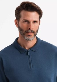 Marineblaues Polohemd aus weichem Stoff, mit einem Reißverschlusskragen und kurzen Ärmeln. Glatte Textur mit lässigem Schnitt.