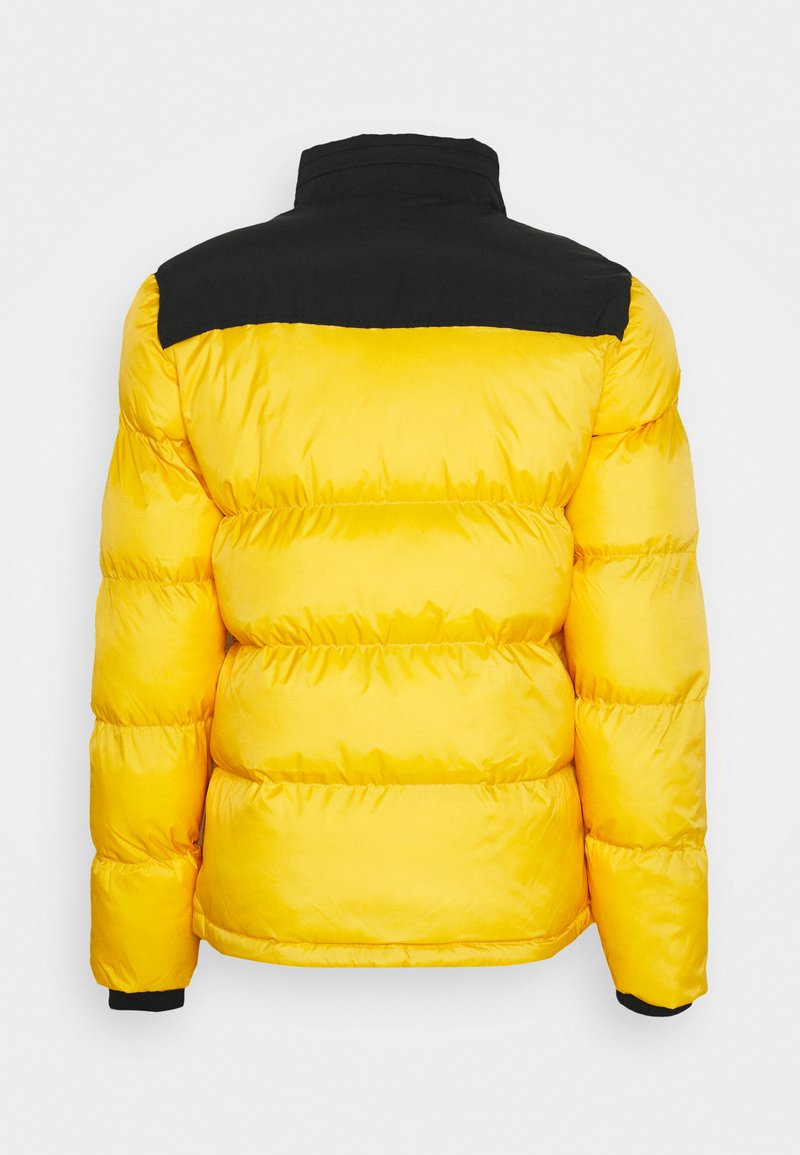 Doudoune jaune avec panneau d'épaule noir, design matelassé, col haut et poignets élastiques. La texture semble lisse et brillante.