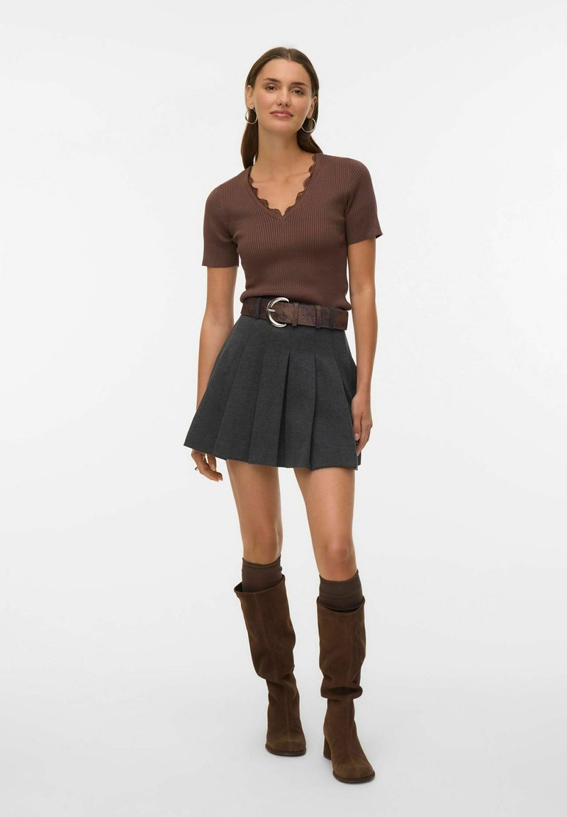 Pruun soonikkoes lühikeste varrukatega top lainelise kaelusega, hall volditud seelik, pruun vöö ümmarguse pandlaga ja pruunad põlve kõrged saapad.