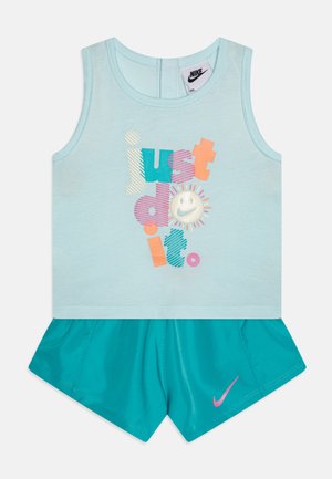 Svetlo modrá tielko bez rukávov s viacfarebným textom a grafikou usmievajúcej sa tváre, skombinované s tehlovými šortkami s ružovým logom Nike.