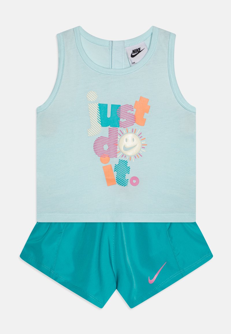 Top sem mangas azul claro com texto multicolorido e um gráfico de smiley, combinado com calções turquesa com um logo da Nike em rosa.