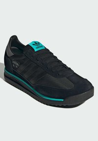 Black athletic shoe with a smooth suede and textile upper. Features a turquoise accent, three black stripes, and a padded tongue.