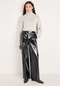 Camisola de gola alta cinza clara com nervuras, combinada com calças pretas de couro sintético de cintura alta e perna larga, e sapatos pretos de bico fino com detalhes de ilhós.