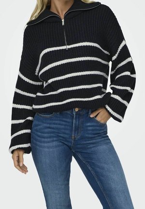 Knitted pullover with a half-zip collar, featuring navy and white stripes. Relaxed fit with wide sleeves, paired with light blue jeans.