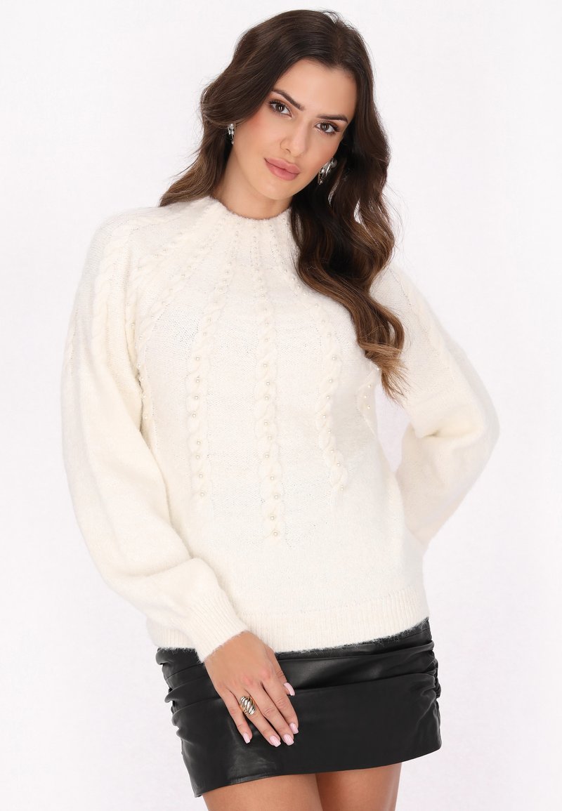 Maglione bianco lavorato a maglia con un motivo testurizzato e maniche a palloncino, abbinato a una mini gonna di pelle nera. Accentuato con piccoli dettagli decorativi.