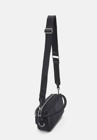 Czarna torba na ramię z materiału, z zapięciem na zamek błyskawiczny, w kształcie prostokąta, z regulowanym paskiem i boczną rączką. Posiada metalowe akcenty.