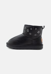 Bottines noires en cuir avec une texture lisse, dotées d'accents en œillets et d'une semelle en caoutchouc plate. Comprend une languette à l'arrière.