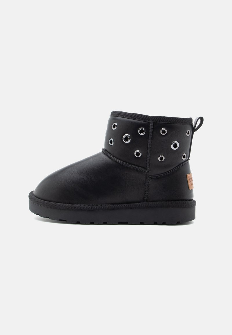 Bottines noires en cuir avec une texture lisse, dotées d'accents en œillets et d'une semelle en caoutchouc plate. Comprend une languette à l'arrière.