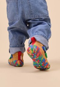 Bunte Kinderschuhe mit einer strukturierten Sohle, die eine Mischung aus roten, blauen und grünen Akzenten aufweisen. Hergestellt aus weichem, hellbraunem Material mit lebhaften Mustern.